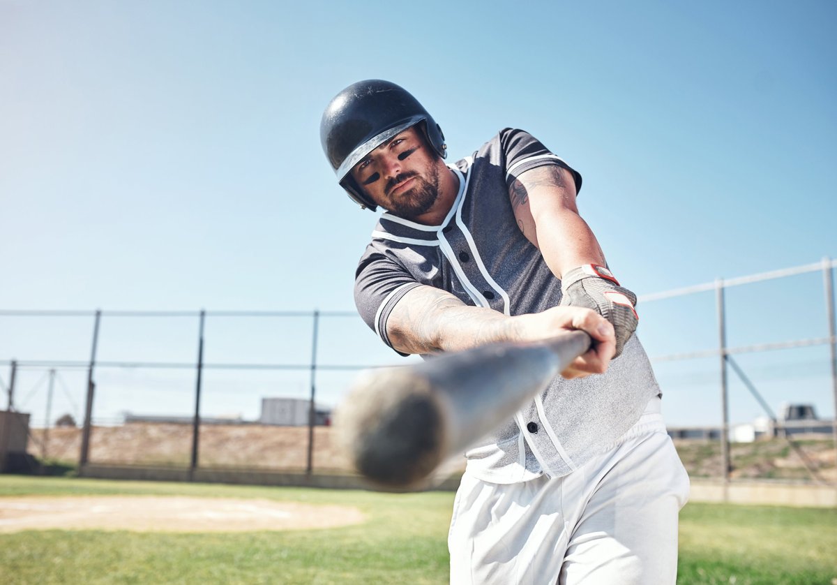 College baseball player swinging a bat at a game on a sunny field