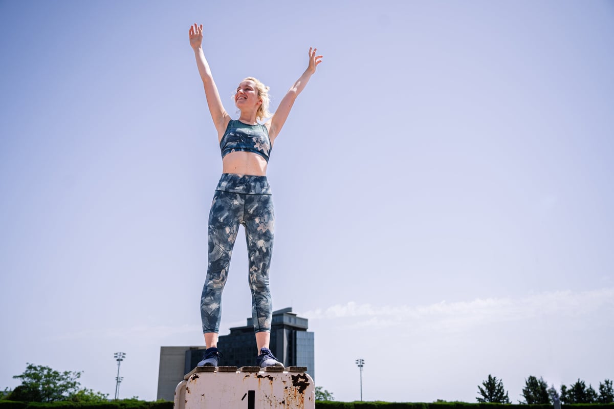 Young sportswoman in activewear raising arms on first place podium against blue sky