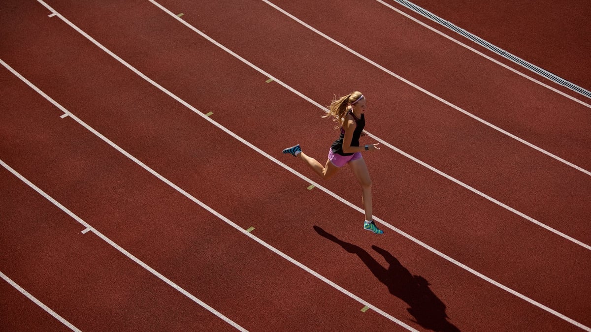 Aerial view of a female athlete sprinting on a red running track on a sunny day
