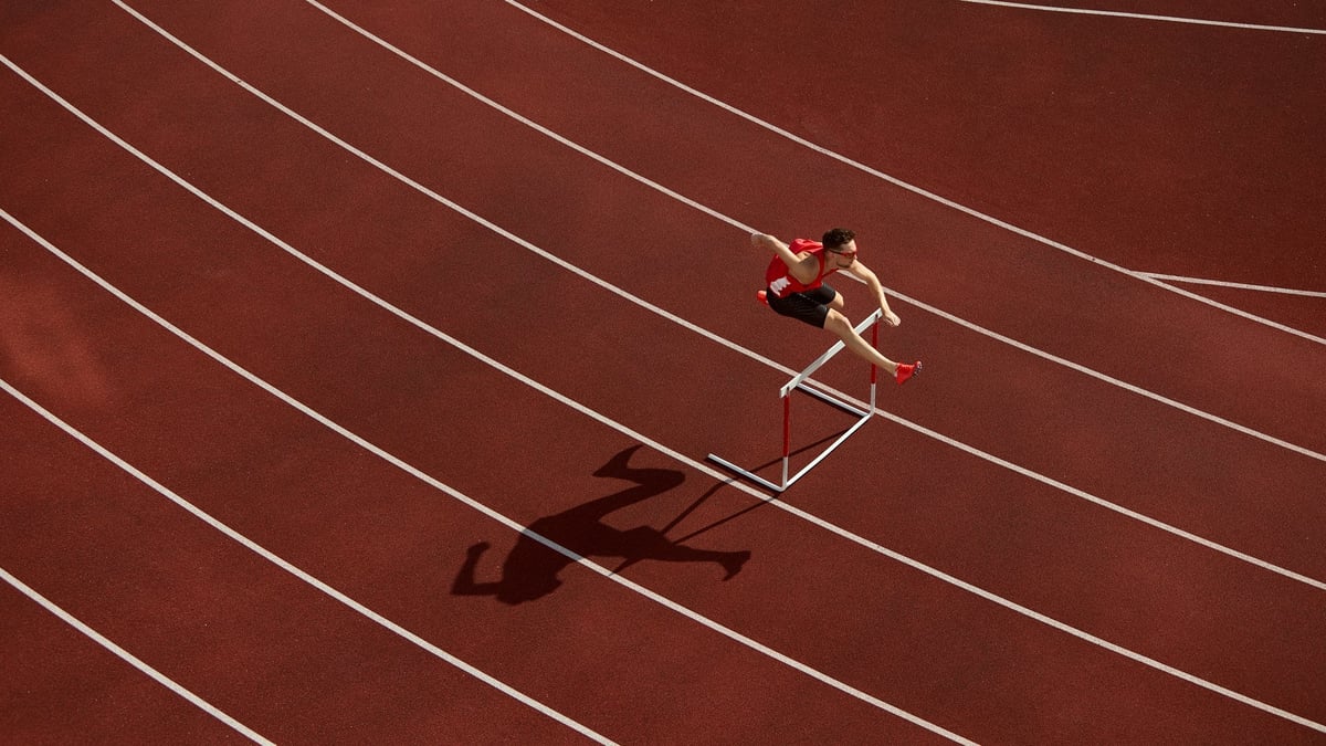 Aerial view of athlete jumping over hurdle on red running track with shadow