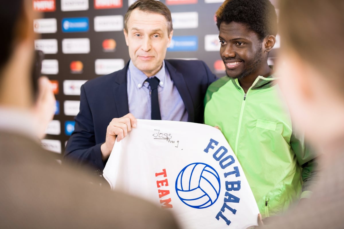 Portrait of a smiling athlete posing with his coach and holding a signed t-shirt