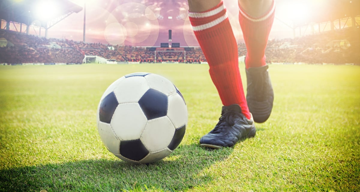 Soccer player preparing to kick a ball on a grassy field in a sunlit stadium