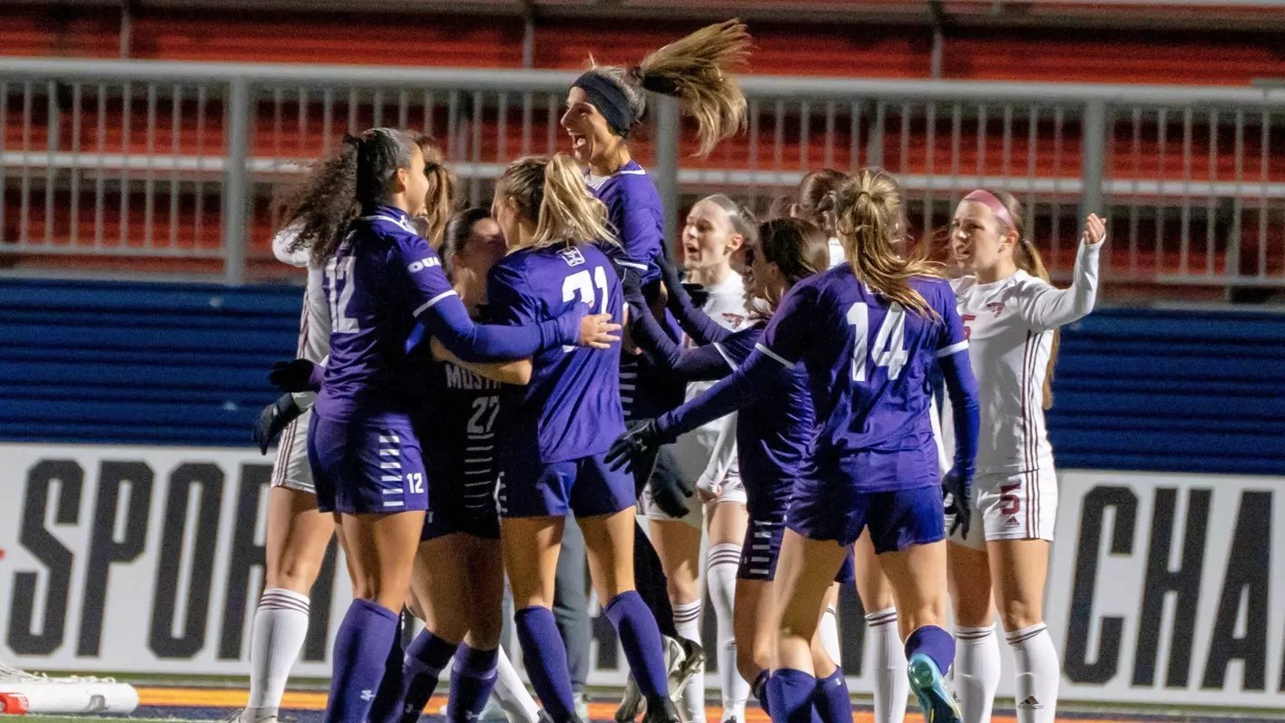 Womens soccer team in purple uniforms celebrating together on field during night game