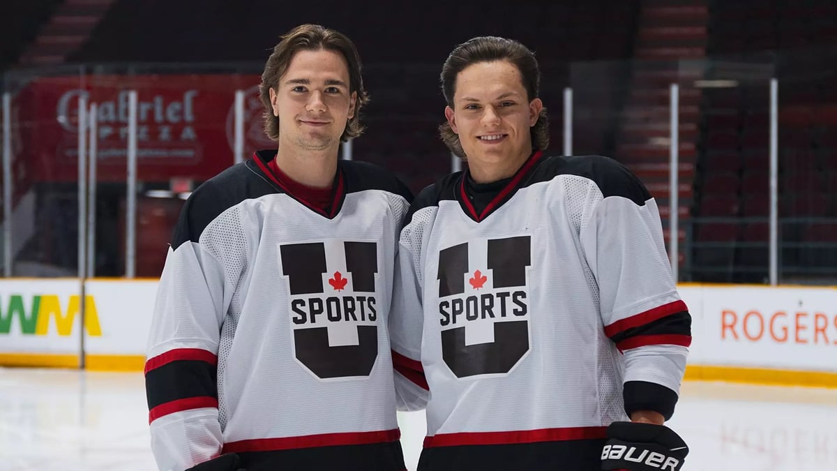 Two hockey players in white U Sports jerseys standing together on the ice with their arms around each other